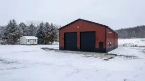 Red metal garage with two doors on a snowy Canadian driveway.