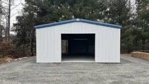 White metal garage with blue trim on gravel lot, front view.
