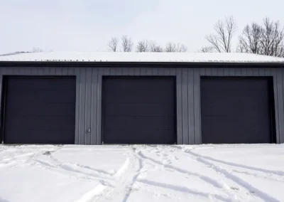 Front view of a 24x36 triple car steel garage with snow on the ground.