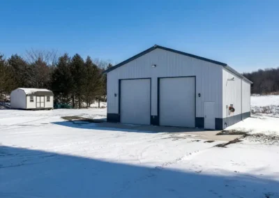 Snow-covered landscape with a large metal garage and smaller shed.