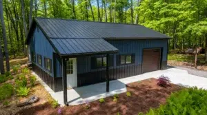Navy blue steel garage with a covered porch in a wooded area.