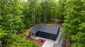 Aerial view of a navy blue steel garage with workshop in a forest setting.