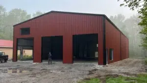 Large red metal garage workshop with three bays in a wooded area